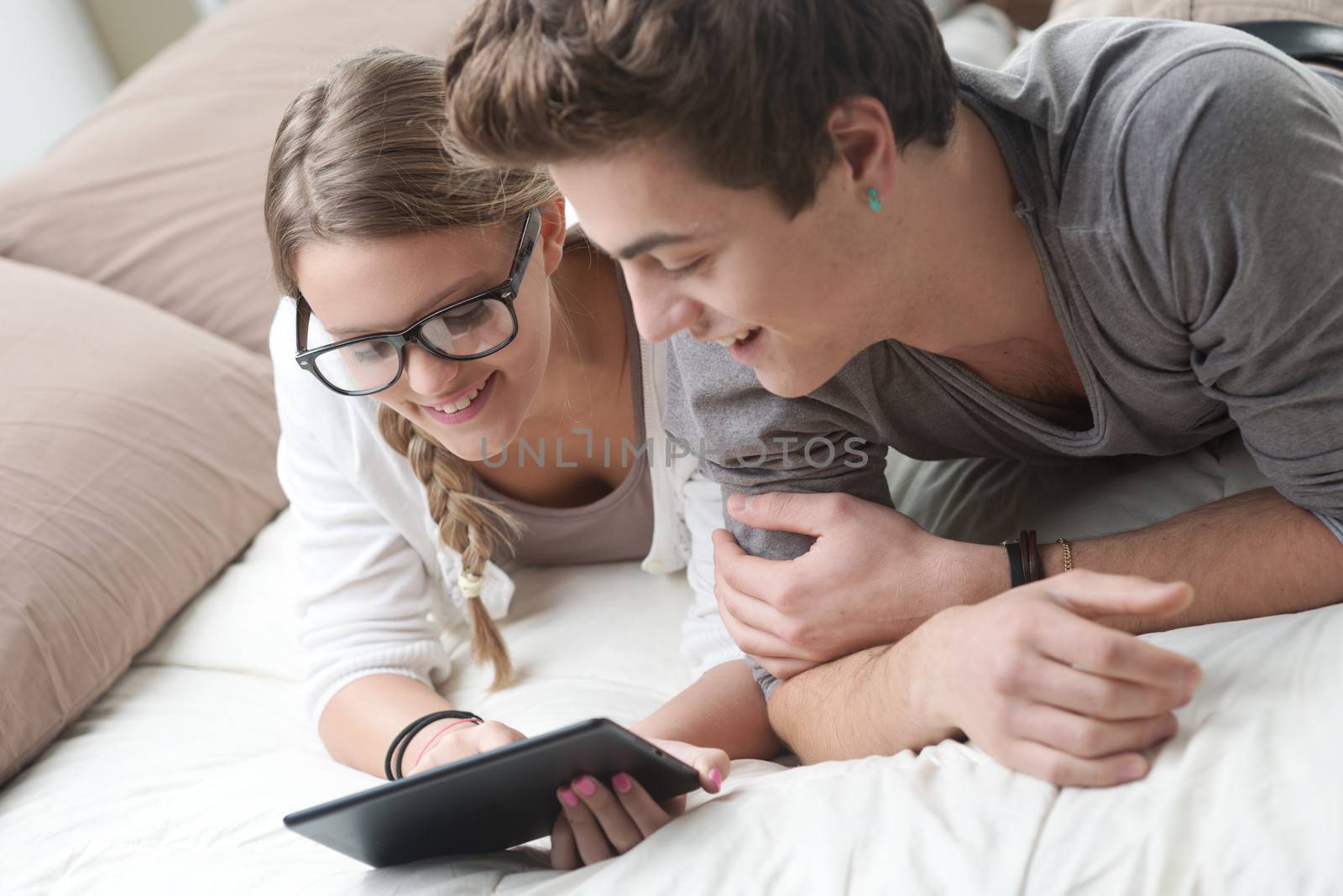 Two happy friends lying in bed using a digital tablet together 