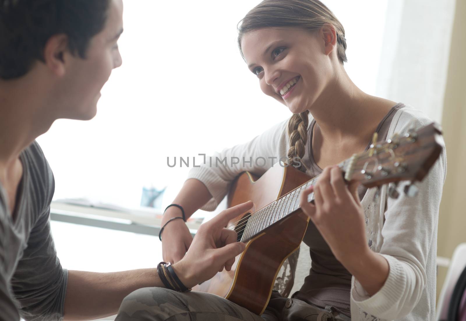 Young beautiful couple resting at home and playing guitar