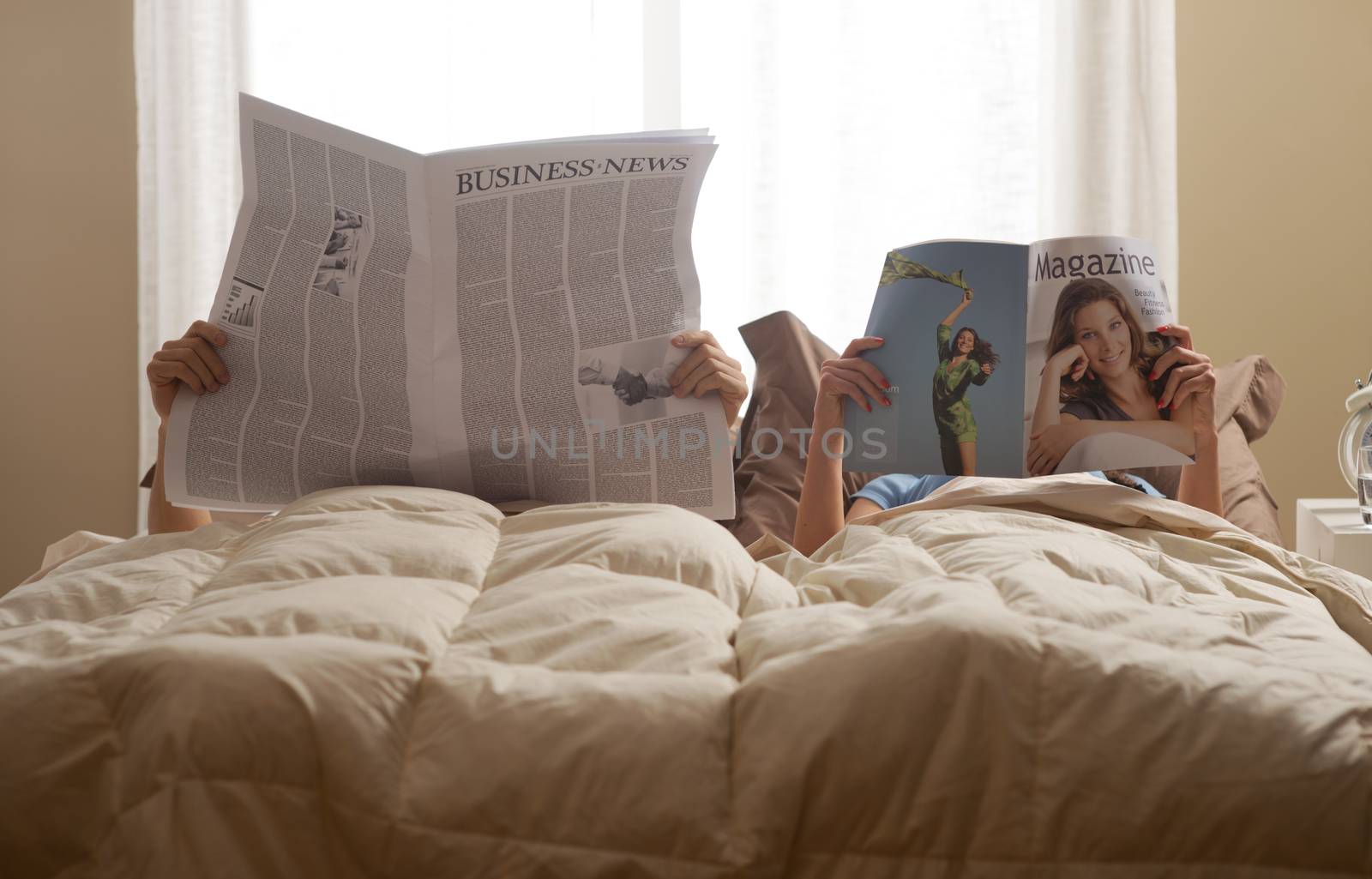 Young couple in bedroom reading newspaper and magazine