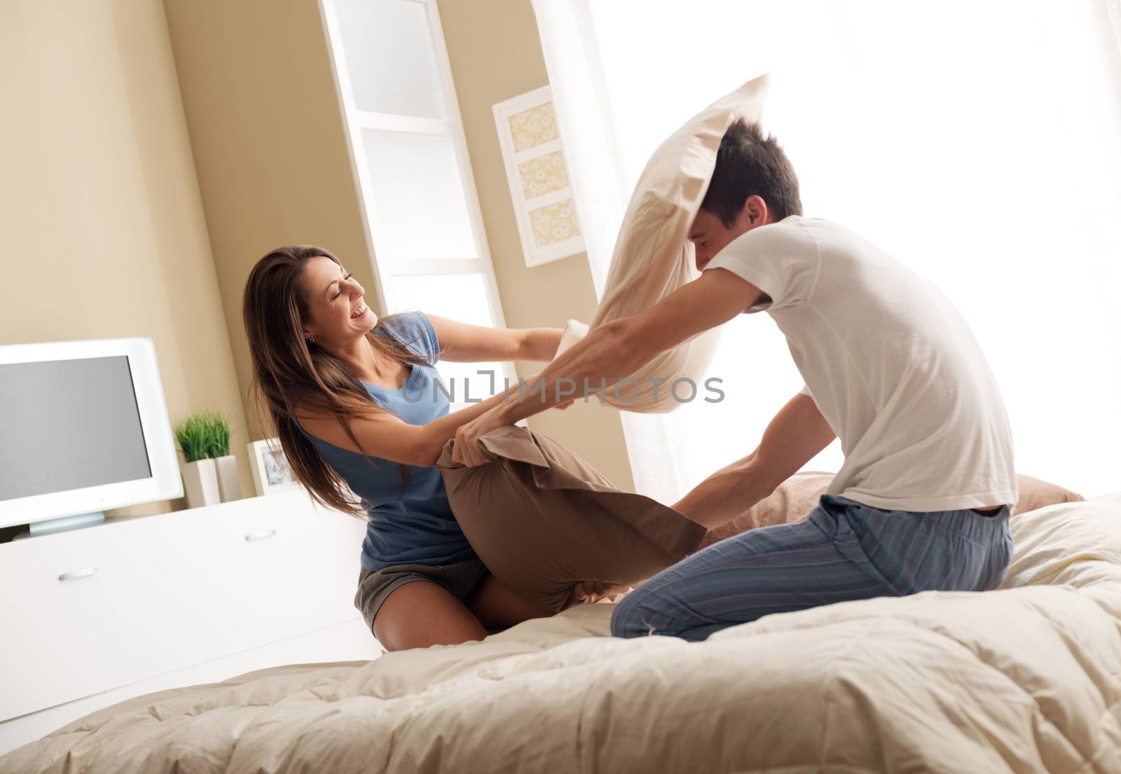 Portrait of happy loving couple having a pillow fight in bed