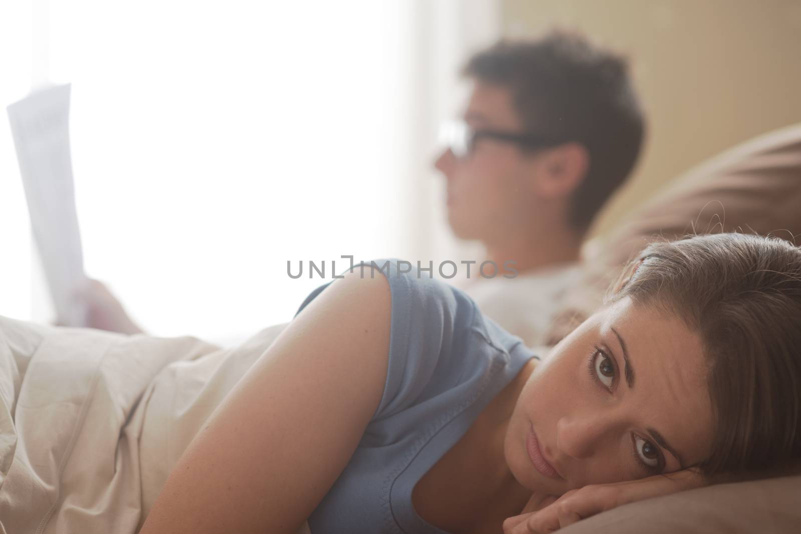 Couple in bed,she's worried while he's reading a newspaper
