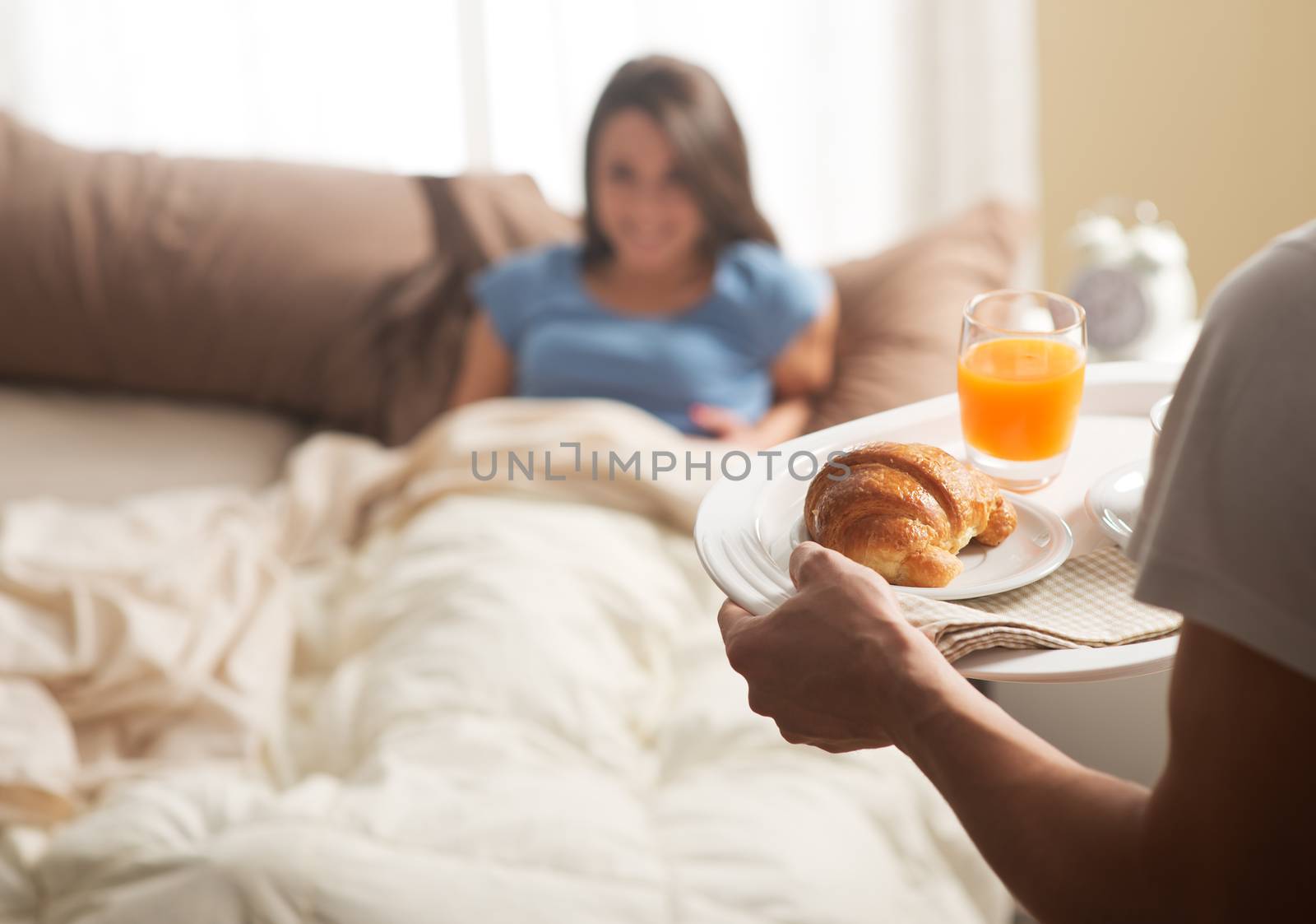 Hand holding breakfast tray to a happy relaxed woman in bed 