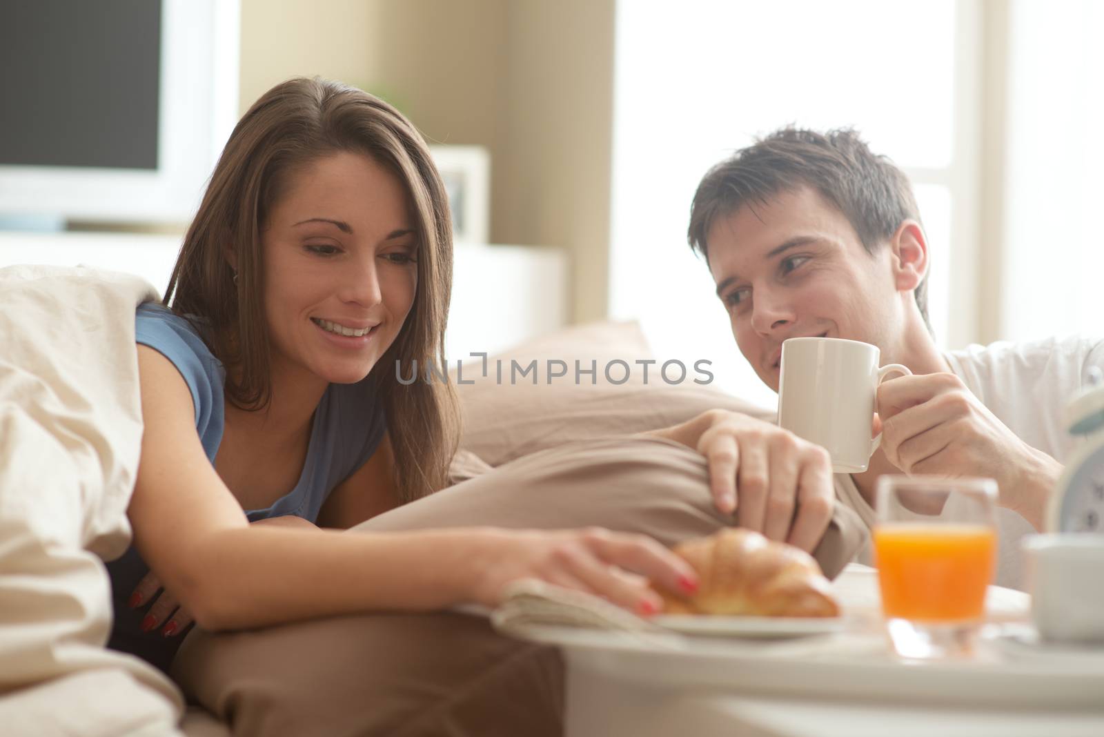 Beautiful smiling young couple having breakfast in bed