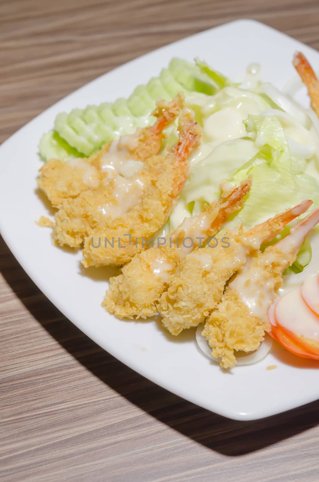deep fried shrimp and  fresh vegetable salad over white dish on wooden table
