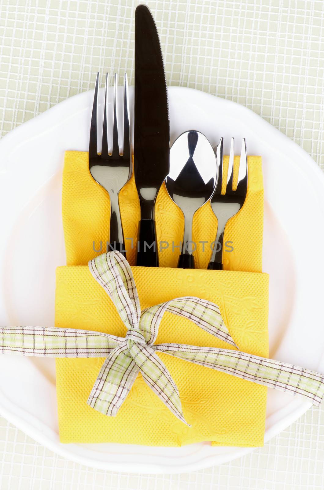 Elegant Table Setting with Fork, Table Knife, Spoon and Dessert Fork into Yellow Napkin Decorated with Green Checkered Bow on White Plate