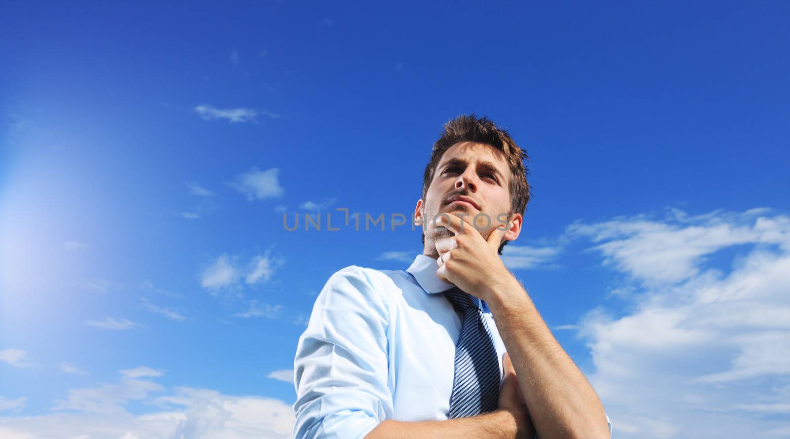 Young business man looking up against a blue sky