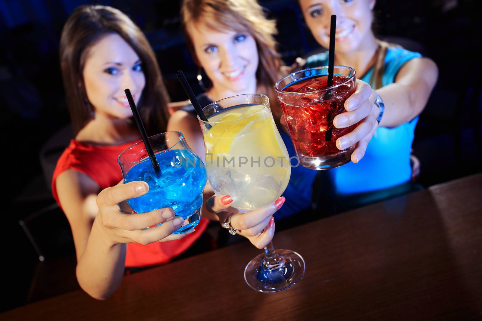 Group of happy beautiful young female friends celebrating in a nightclub with glasses of cocktail in their hands