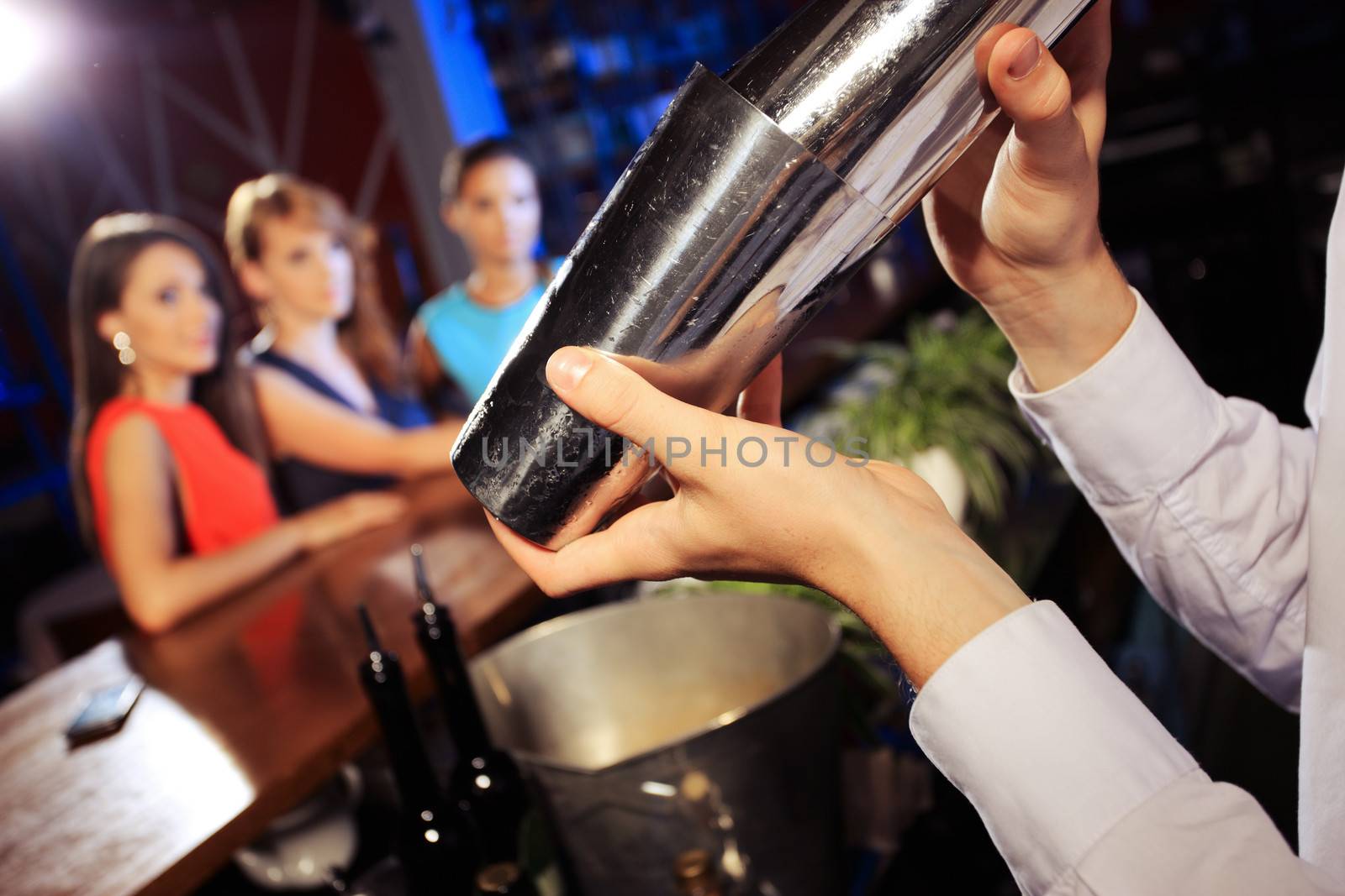 Waiter shaking a cocktail, young women on the background