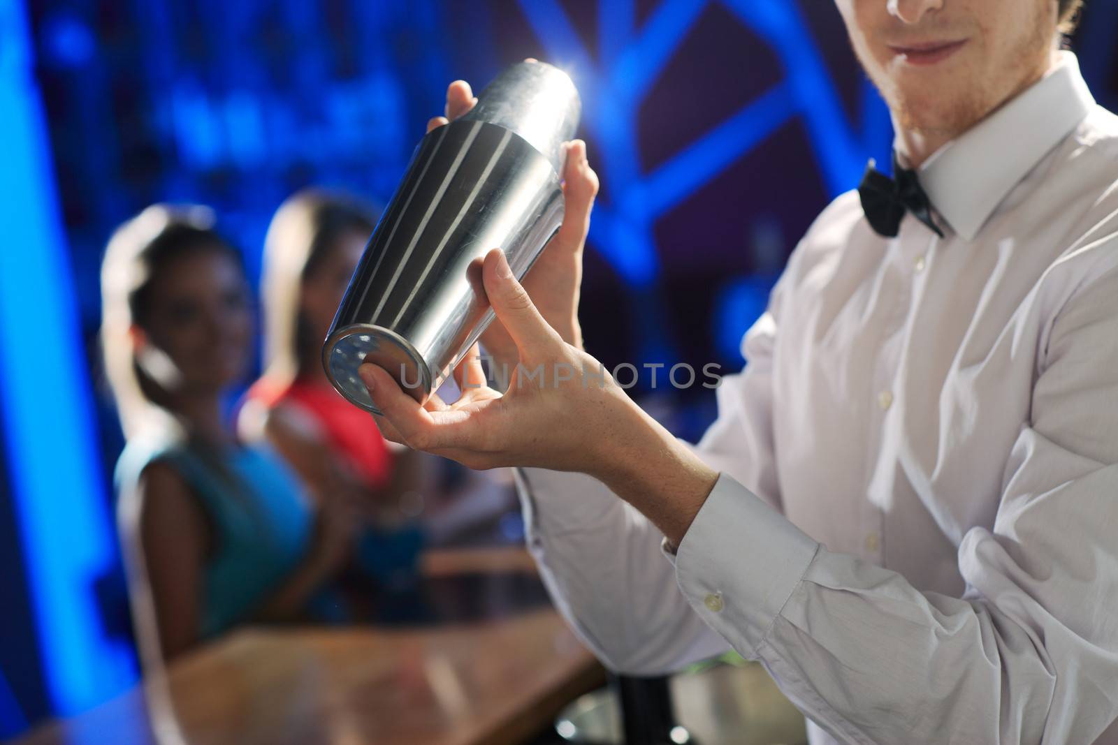 Bartender shaking a cocktail, young women on the background