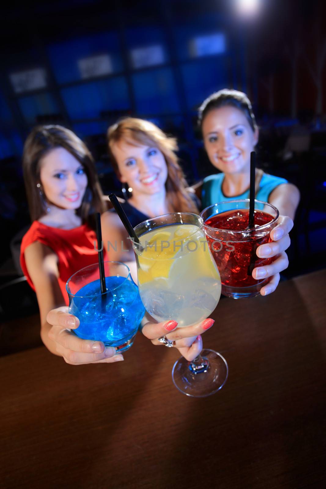 Group of happy beautiful young female friends celebrating in a nightclub with glasses of cocktail, focus on hands