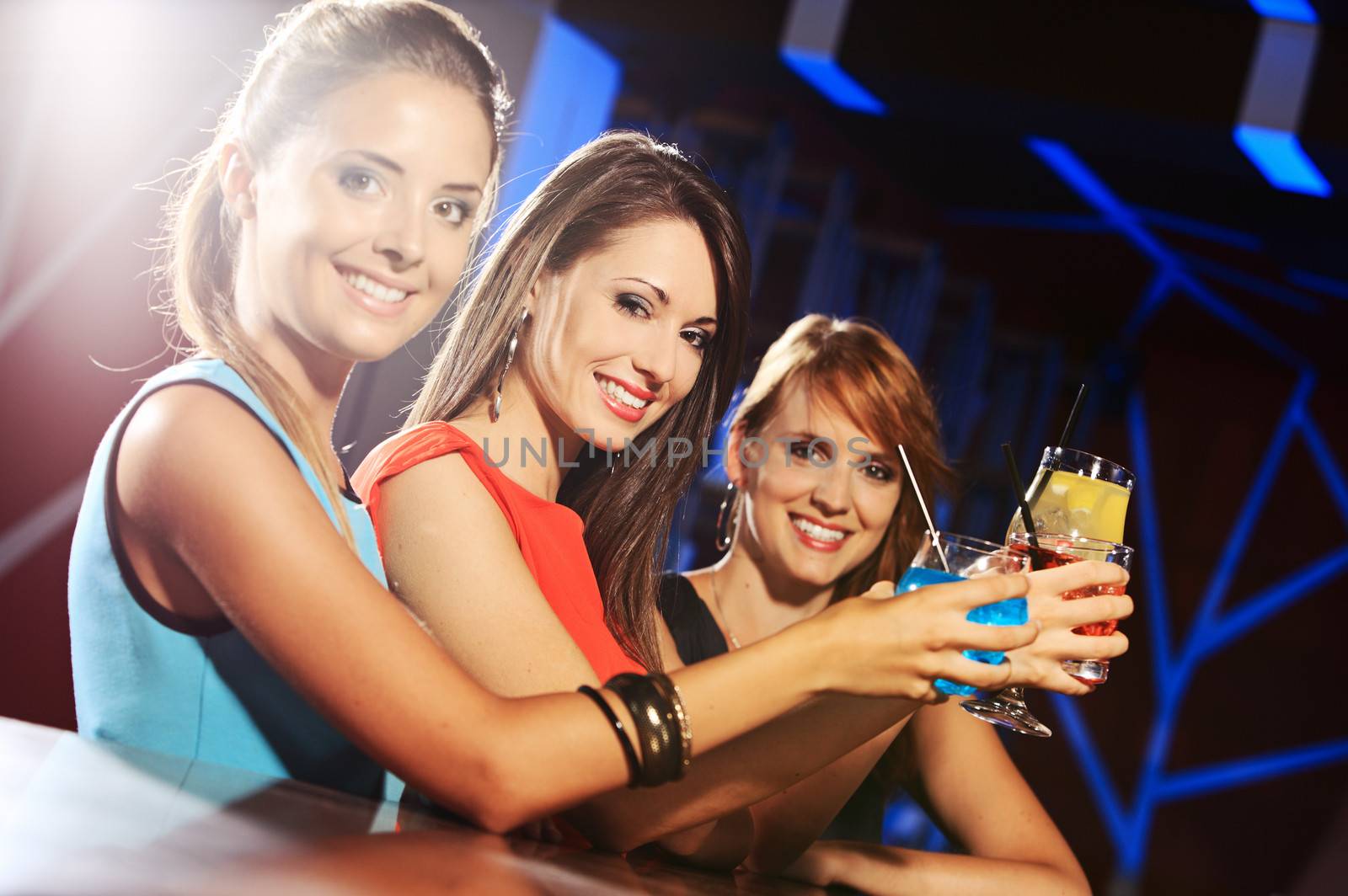 Group of happy beautiful young female friends celebrating in a nightclub with glasses of cocktail in their hands