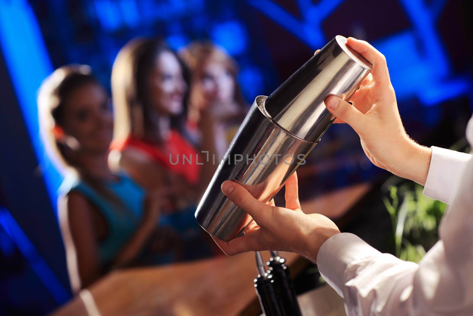 Bartender shaking a cocktail, young women on the background