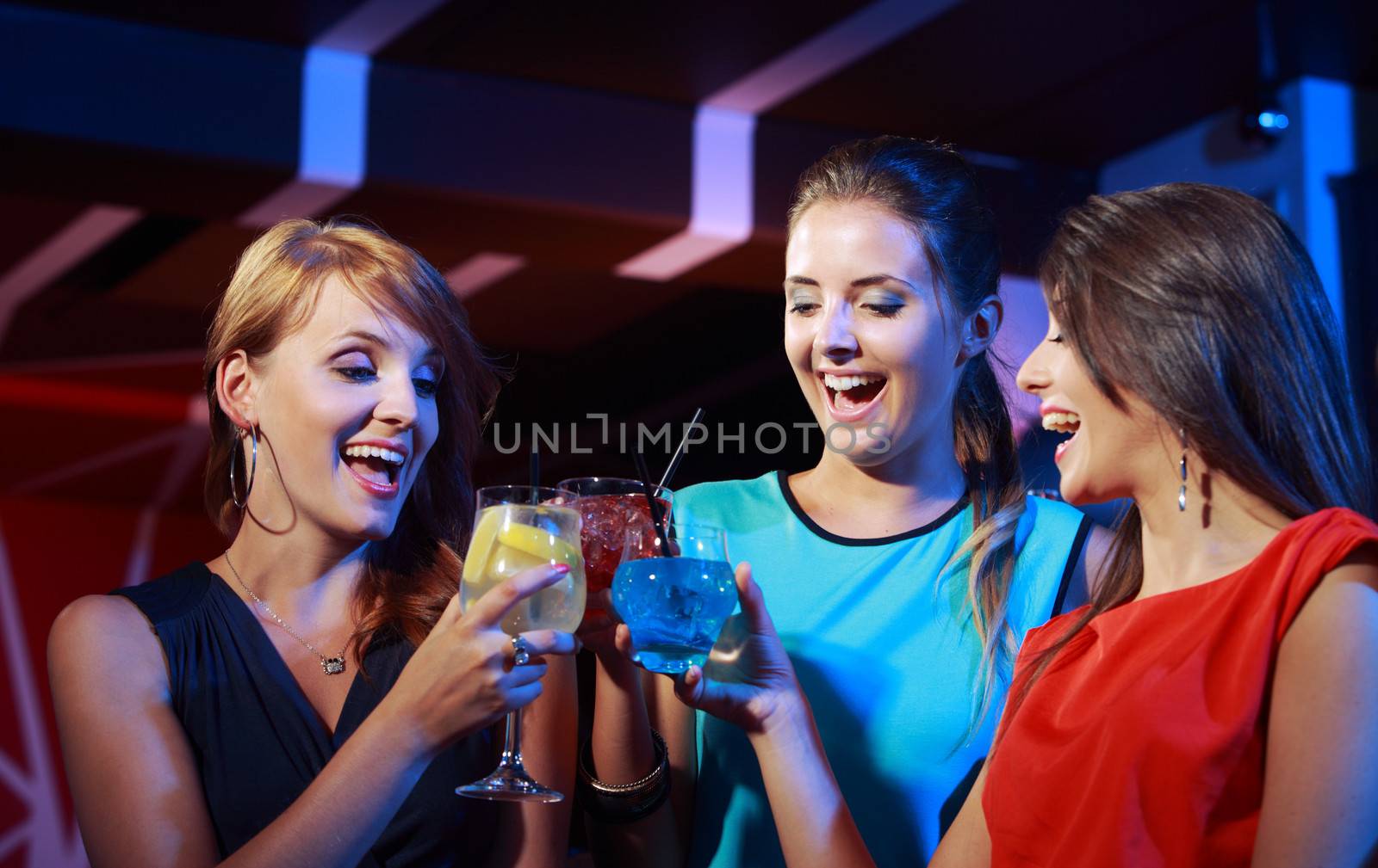 Group of happy beautiful young female friends celebrating in a nightclub with glasses of cocktail in their hands