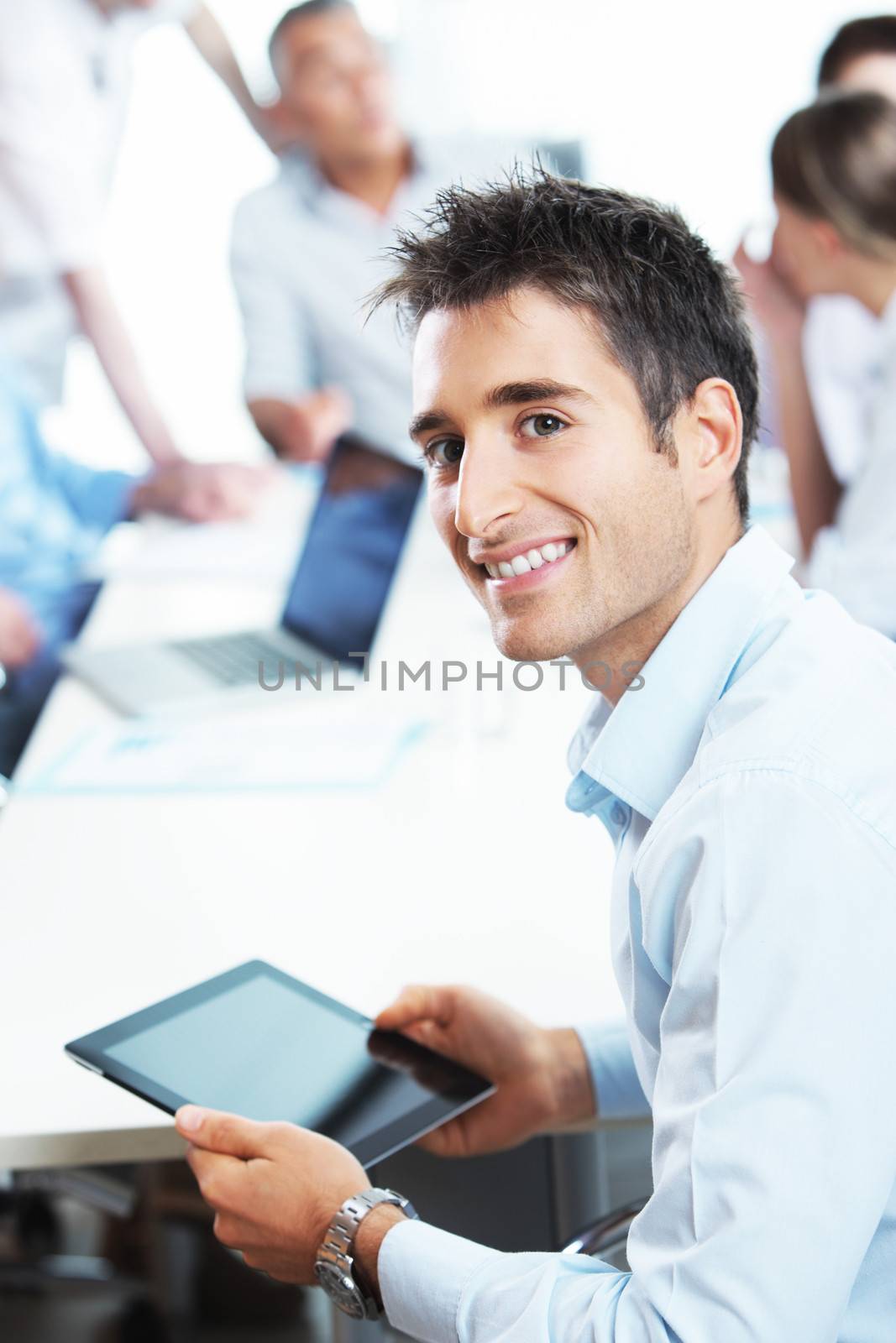 Portrait of a young  businessman using his digital tablet, colleagues in the background 