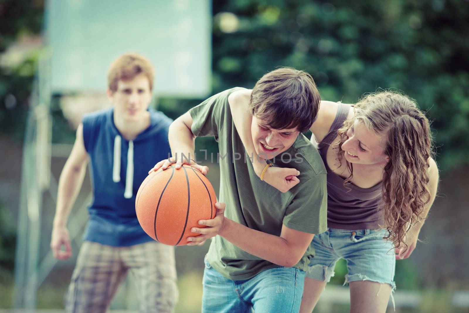 Teens playing a game of basketball on an outdoor court.
