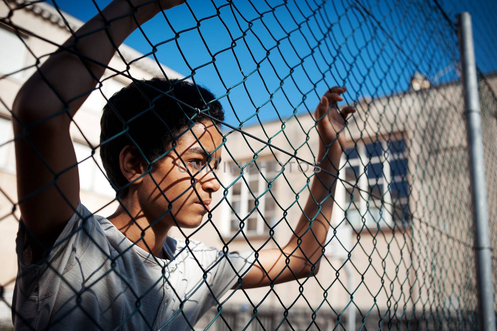 A boy looks  while leaning up against a chain link fence