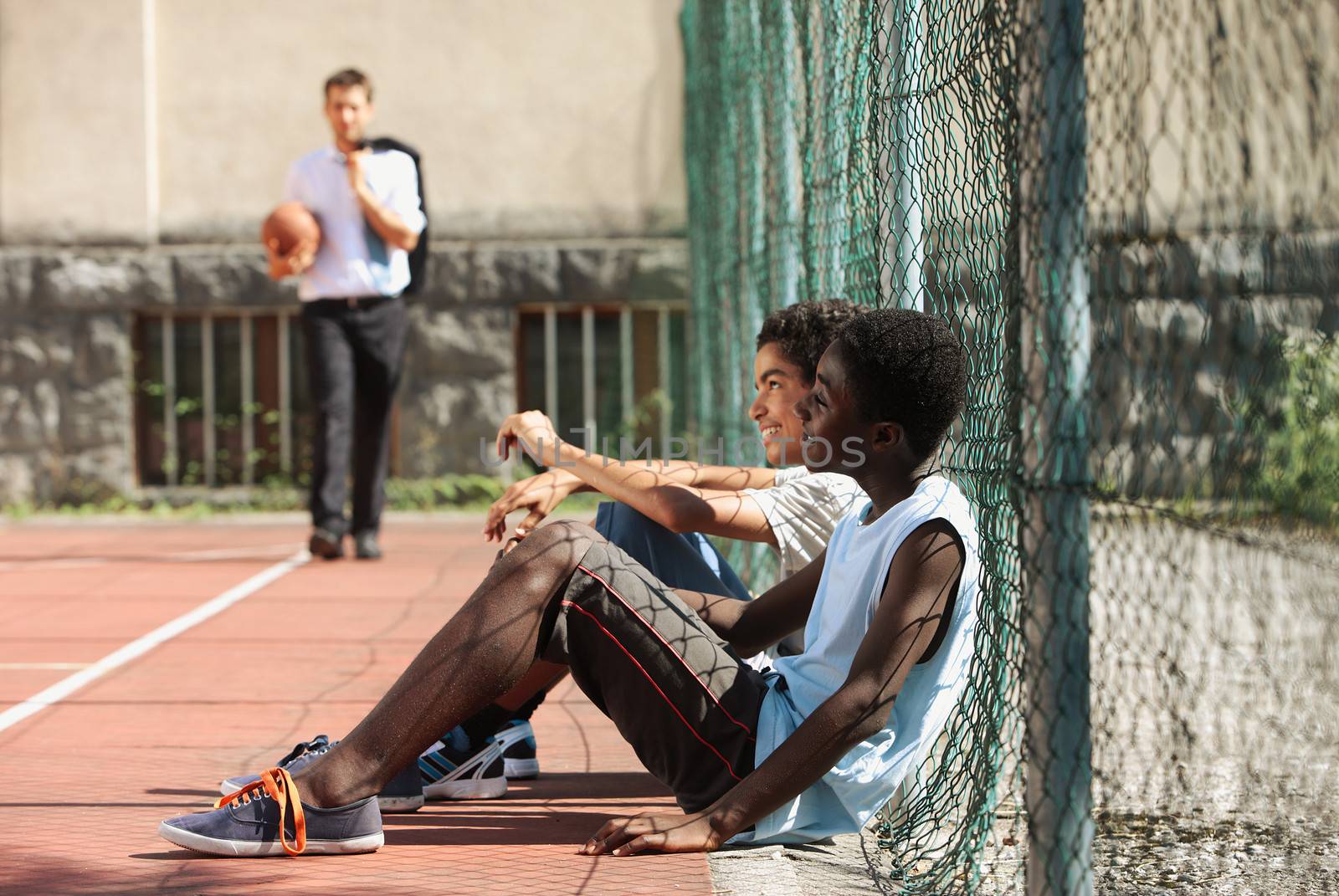 Two boys resting on basketball court young man with basketball on background