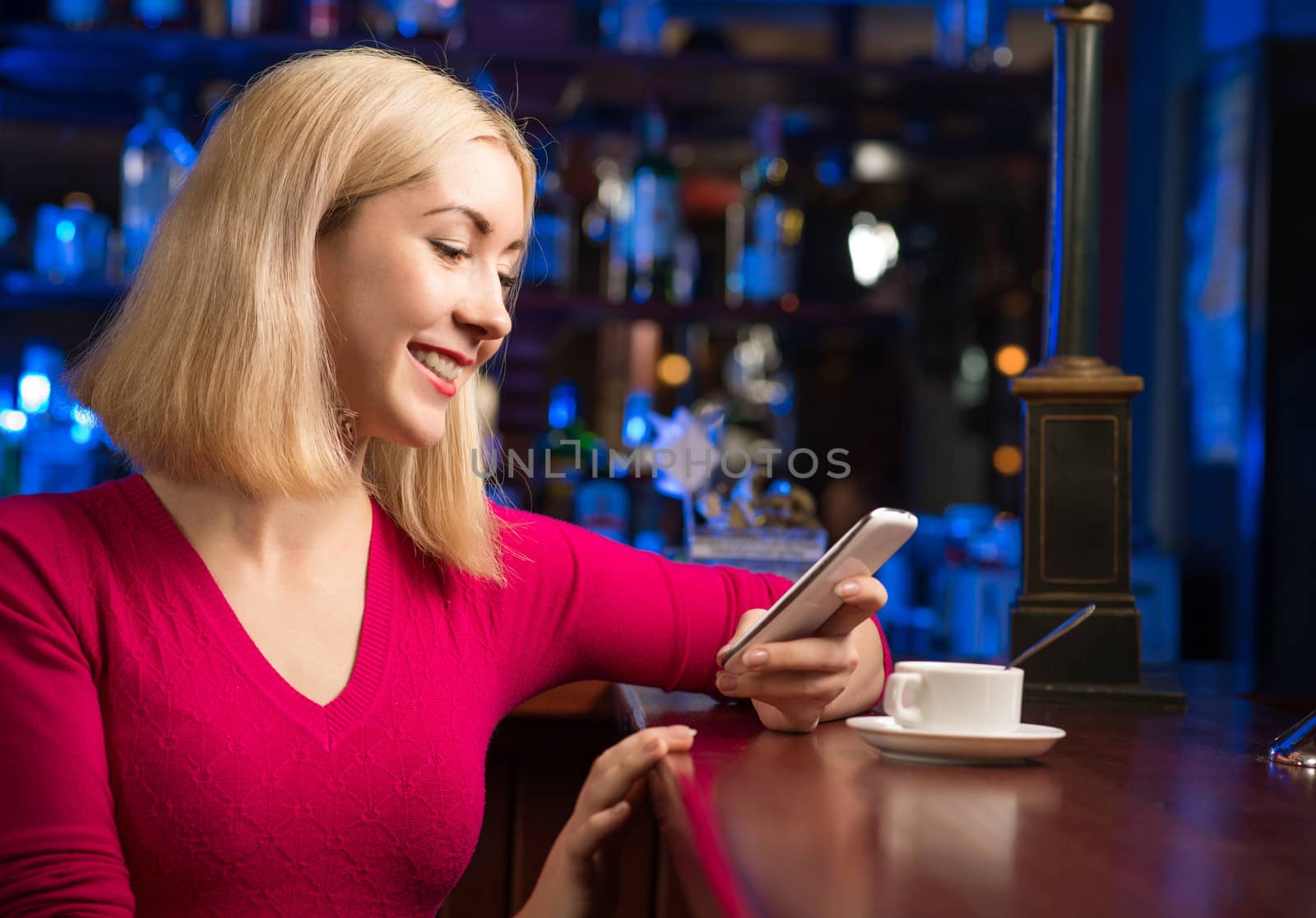 portrait of a young woman in a bar with a cell phone and a cup of coffee