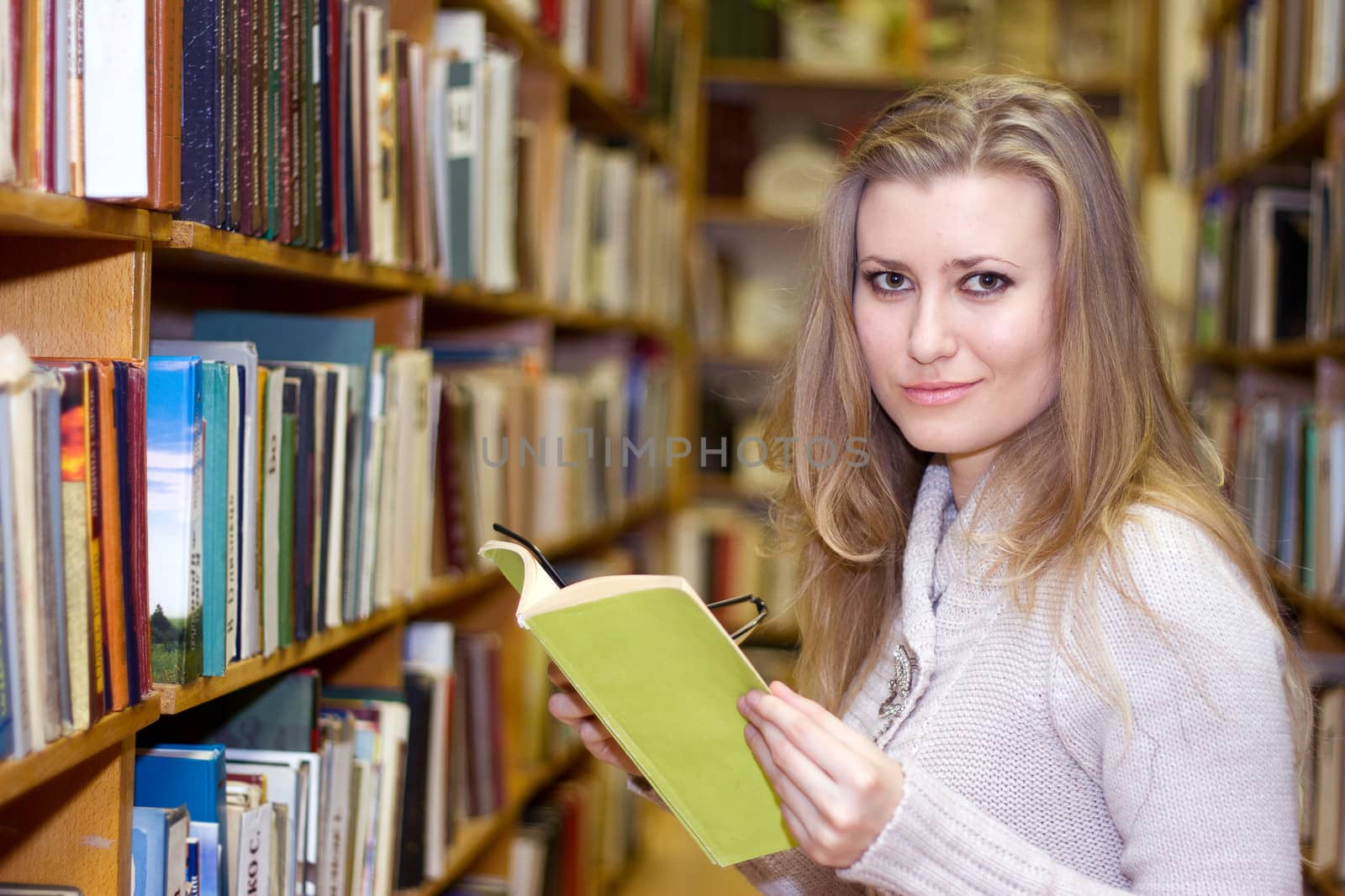 female student standing at bookshelf in old library searching for a book.