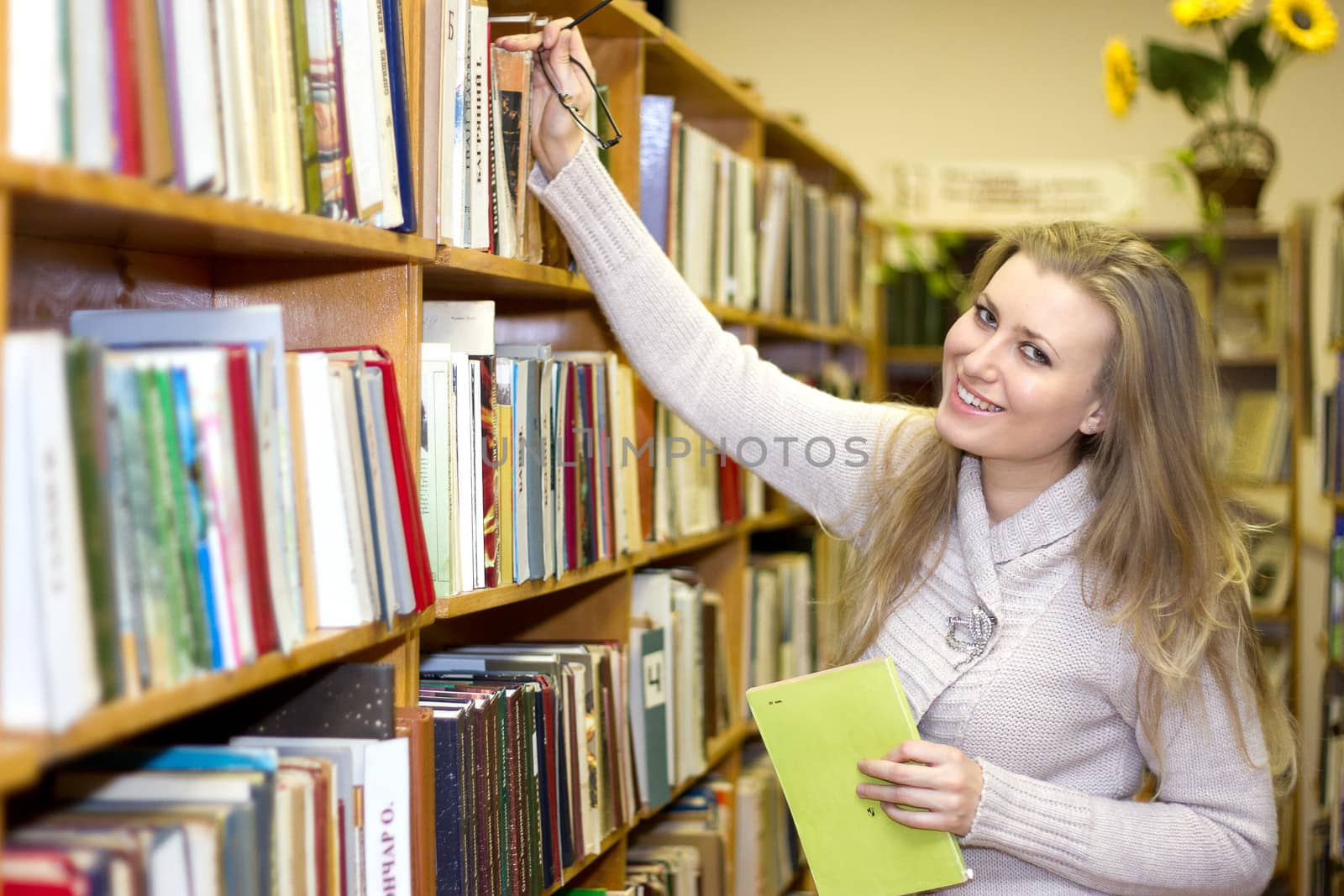 female student standing at bookshelf in old library searching for a book.
