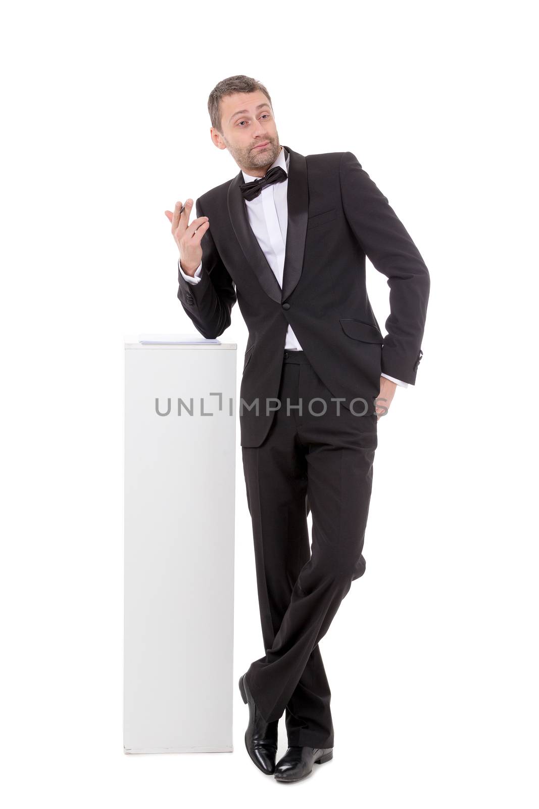 Elegant slender man in a suit and bow tie leaning nonchalantly on a white pedestal with a quizzical charismatic expression