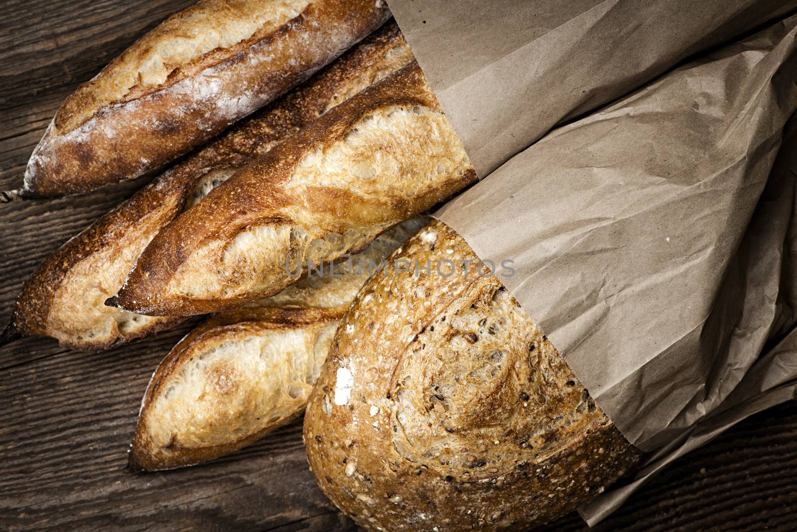 Fresh baked rustic bread loaves in paper bags on dark wood background