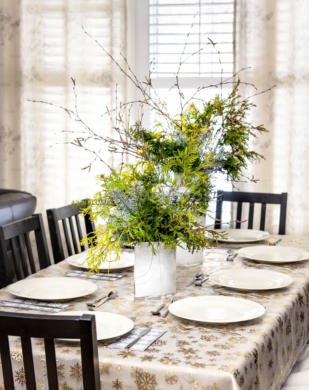 Dining table decorated for Christmas with eight place settings and evergreen centerpiece