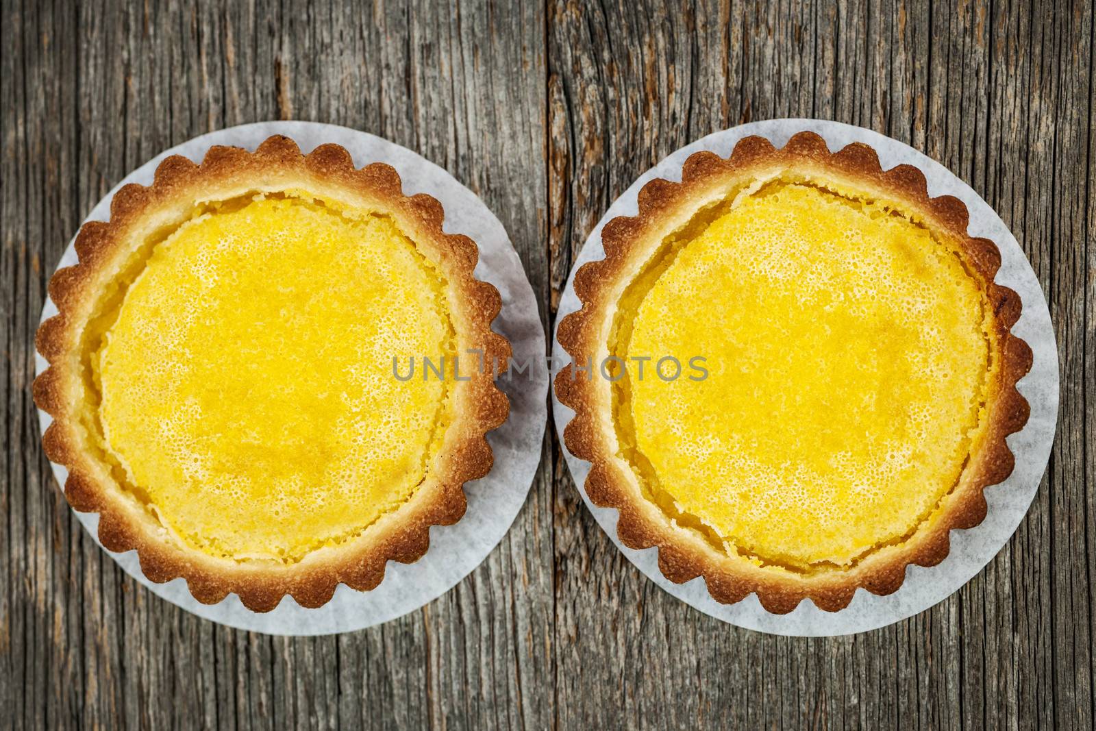 Two fresh gourmet lemon dessert tarts on wood background from above