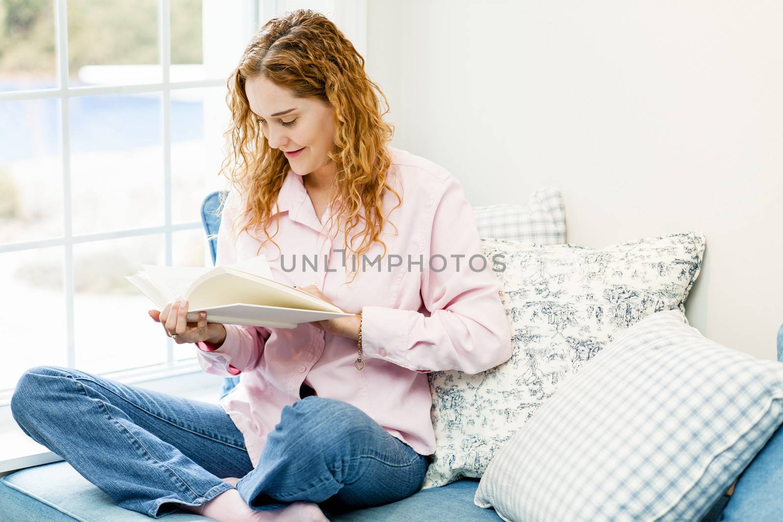 Smiling caucasian woman reading book by window at home