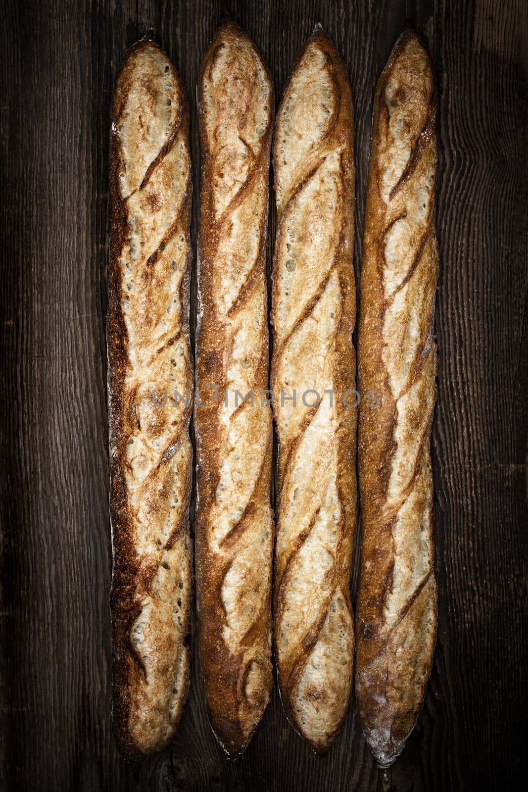 Four whole baguette bread loaves on dark wooden background