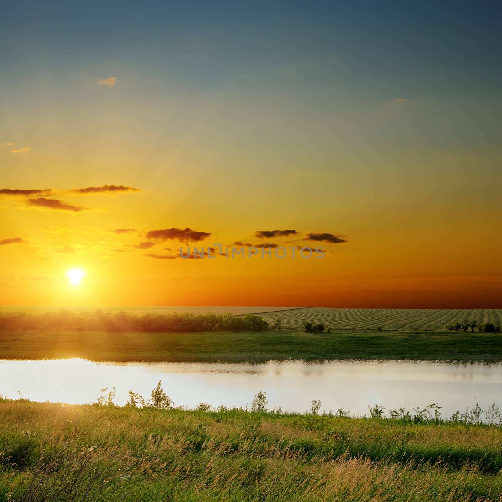 orange sunset over river with green sides