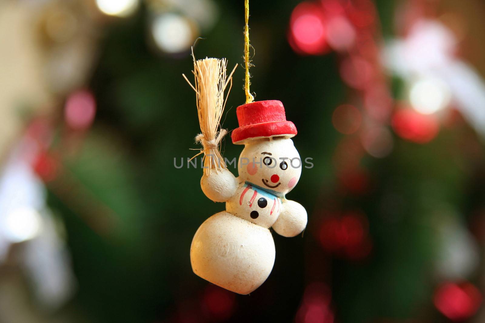 Snowman Christmas tree decoration with red hat and holding sheaf of corn is hanging by a thread  with dark green fir tree background.