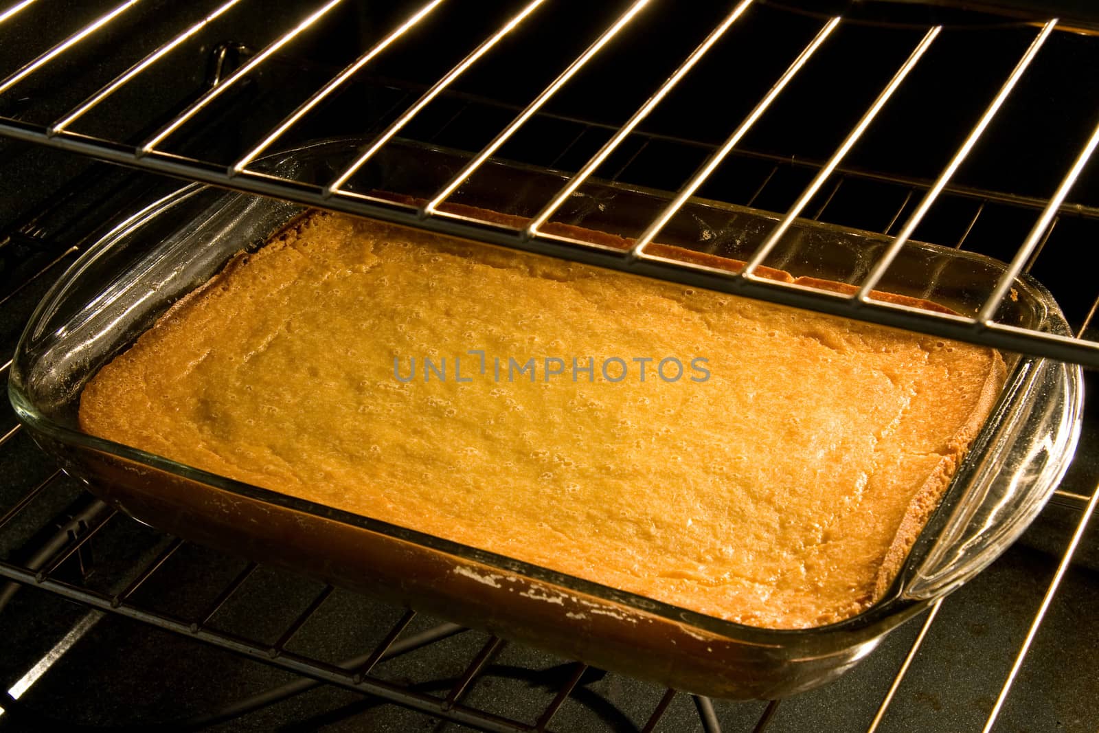 Rectangular glass pan in the oven with cornbread or corn cake.