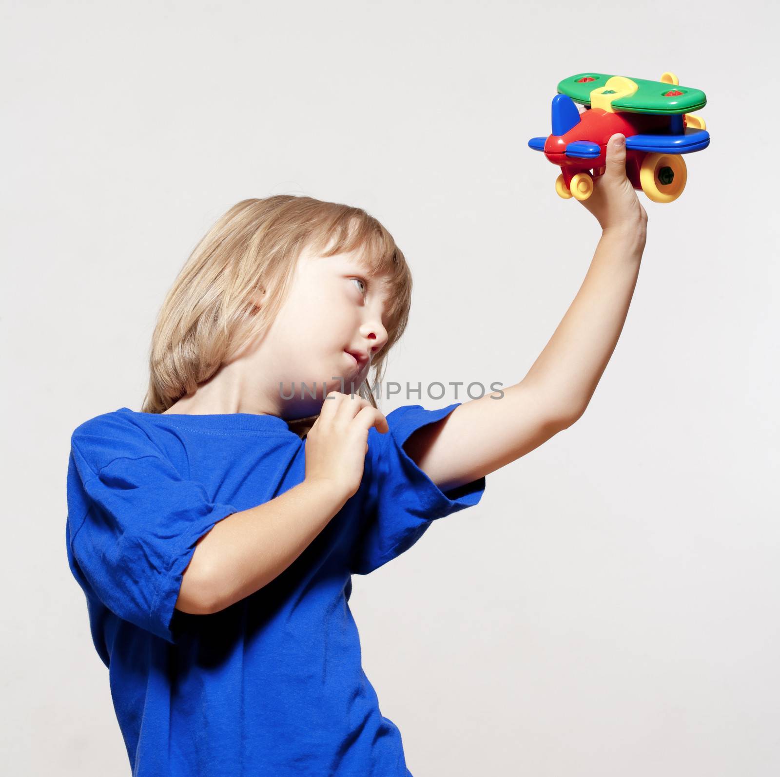 boy with long blond hair playing with toy airplane - isolated on light gray