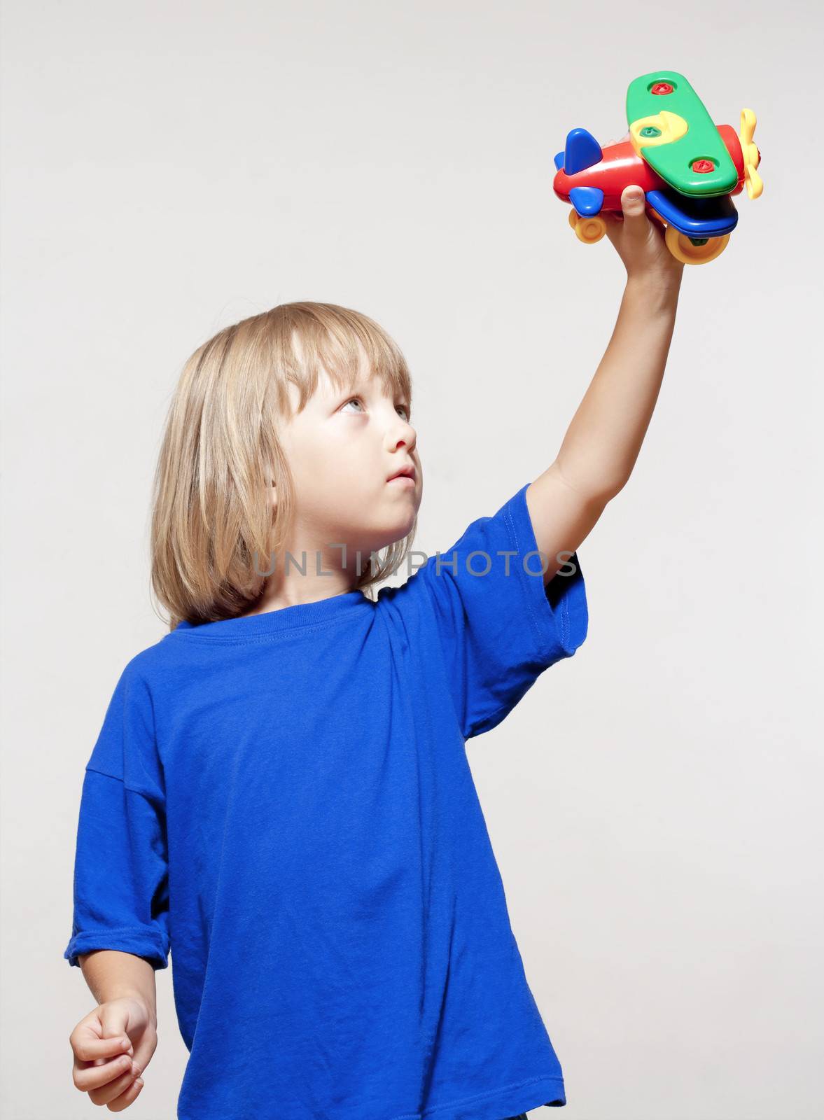 boy with long blond hair playing with toy airplane - isolated on light gray