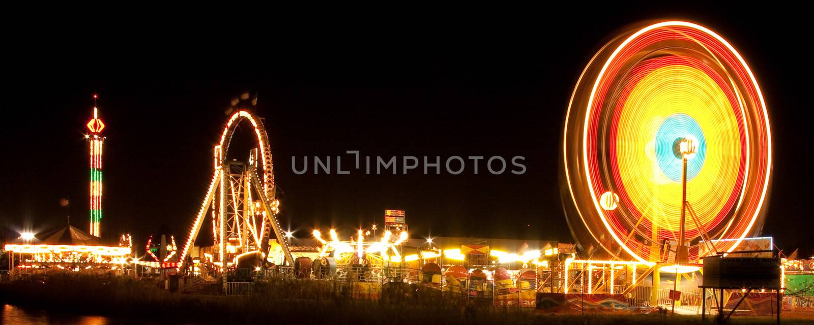 Night shot of a spinning ferris wheel and illuminated rides at a funfair.