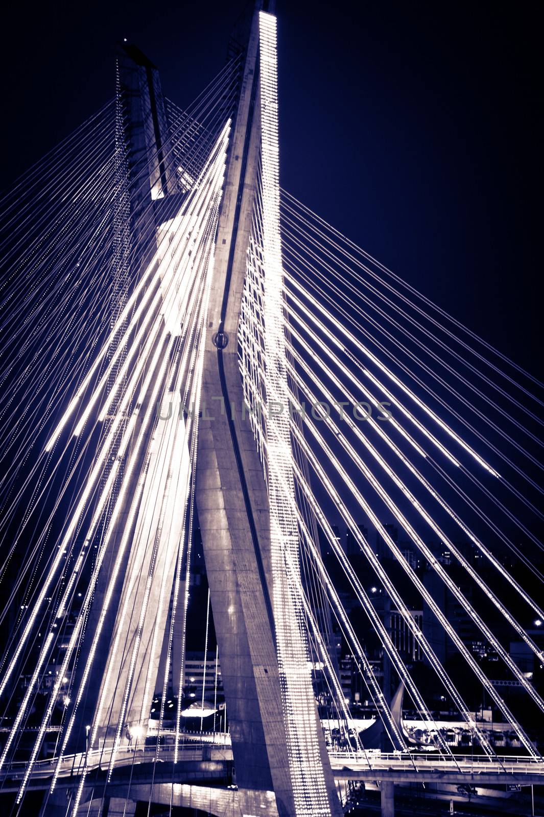 Black and white scenic view of Octavio Frias de Oliveira bridge illuminated at night over Pinheiros river in Sao Paulo, Brazil.