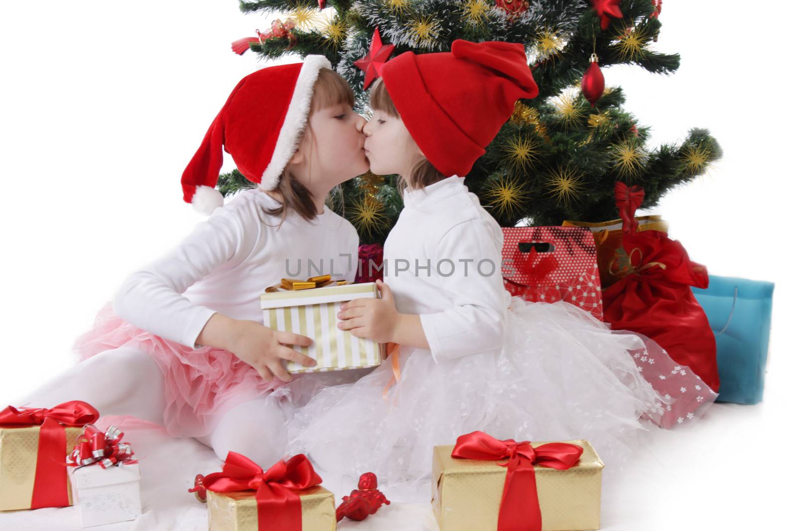 Two little sisters kissing under Christmas tree over white