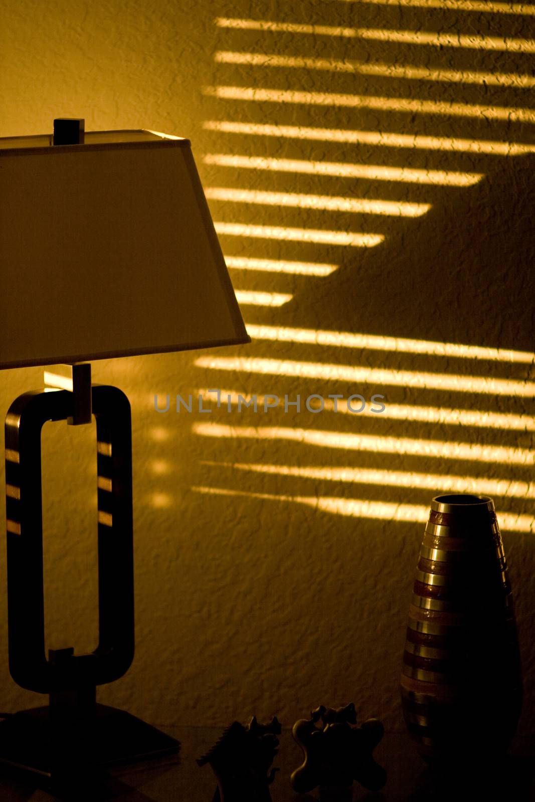 Dark room with stripes of sunshine pattern on the wall. Sun is shining in through window blinds.