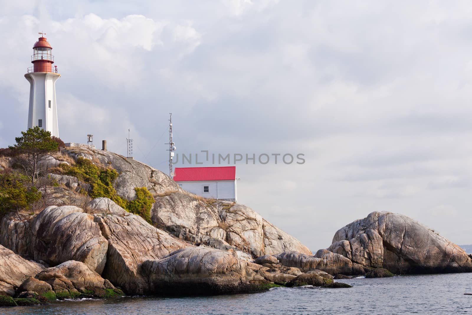 Lighthouse and building with communications antennas on granite rock cliff on British Columbia West Coast north of Vancouver, Canada