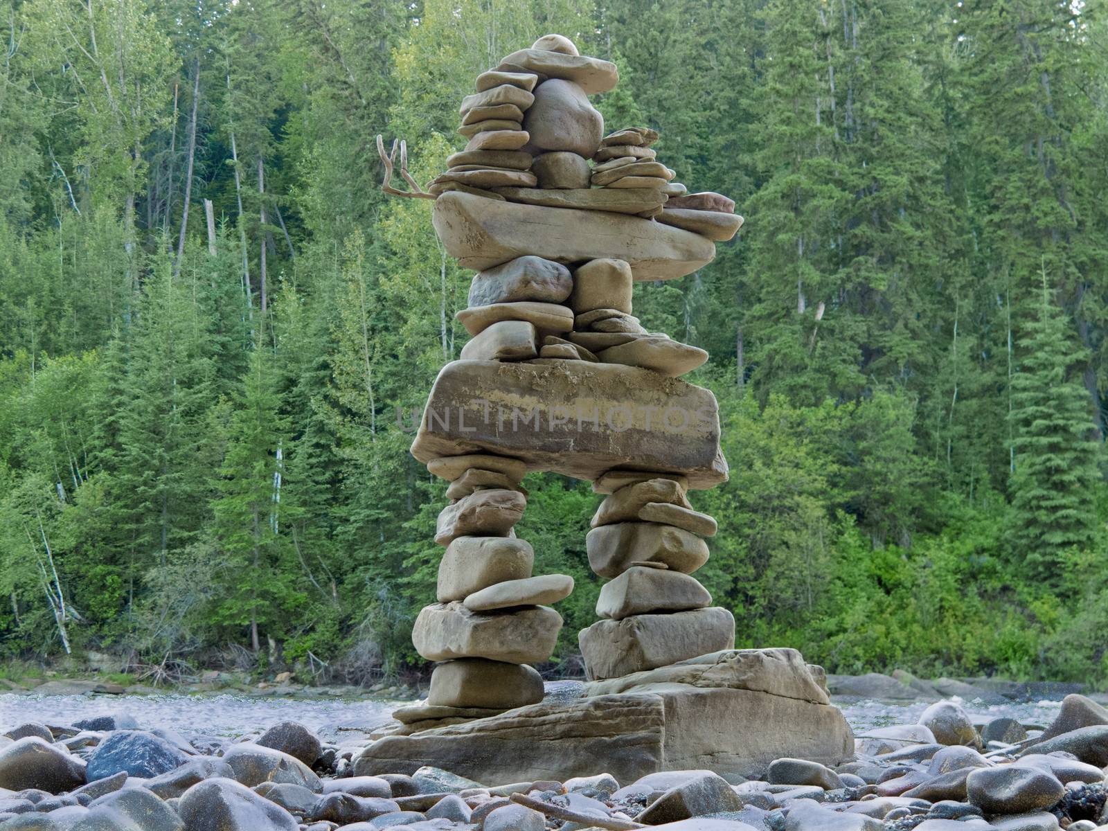 Large rocks stacked and balanced to form an Inuksuk stone landmark or cairn as a marker or monument in front of boreal forest taiga wilderness terrain