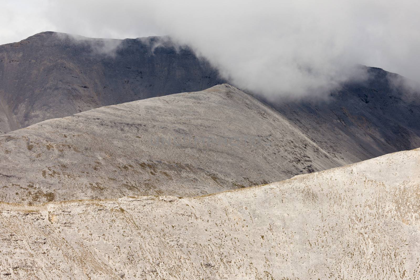 Scenic landscape of rolling mountain ridges, peaks and valleys rocky high alpine terrain with low cloud cover hiding the peak tops of the range