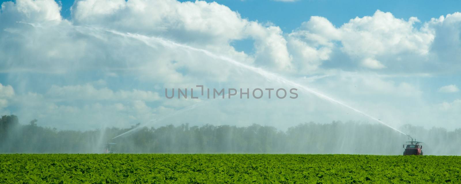 Scenic view of trucks irrigating green field in countryside with cloudscape background.