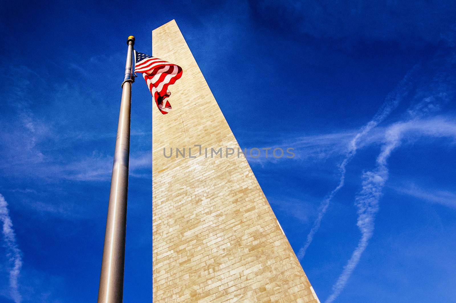 Low angle view looking to top of Washington monument with American flag, blue sky and cloudscape background.