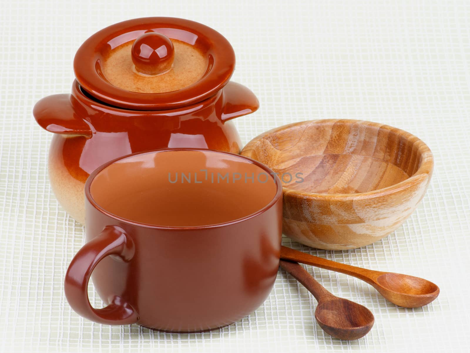 Arrangement Brownish Stoneware Pot, Wooden Bowl, Soup Porringer and Wooden Spoons isolated on Light Green Checkered background