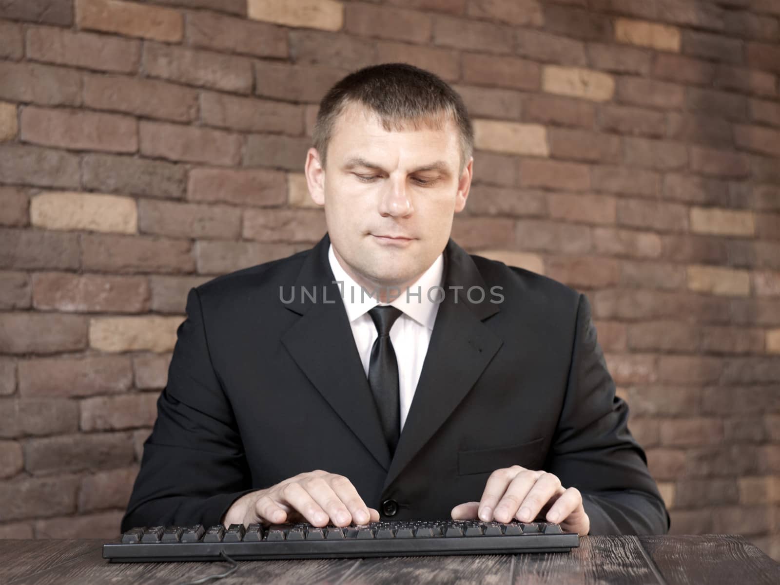 The man in black suit sitting at a desk and looking at the keyboard