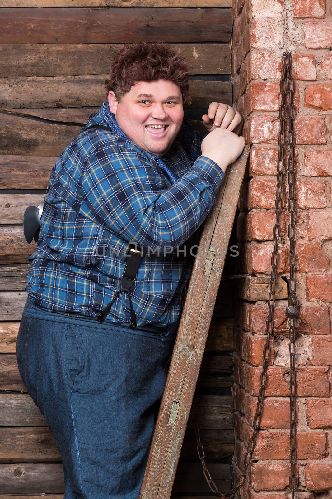 Happy overweight young man standing against a brick wall at the top of a stepladder laughing