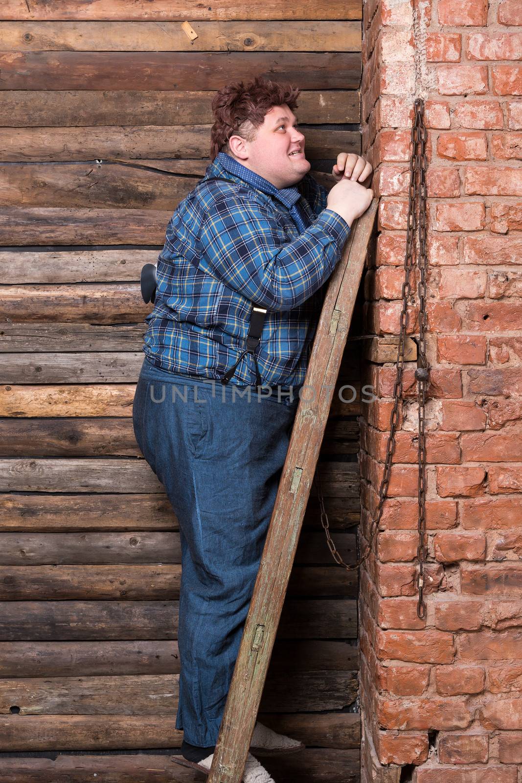 Happy overweight young man standing against a brick wall at the top of a stepladder laughing