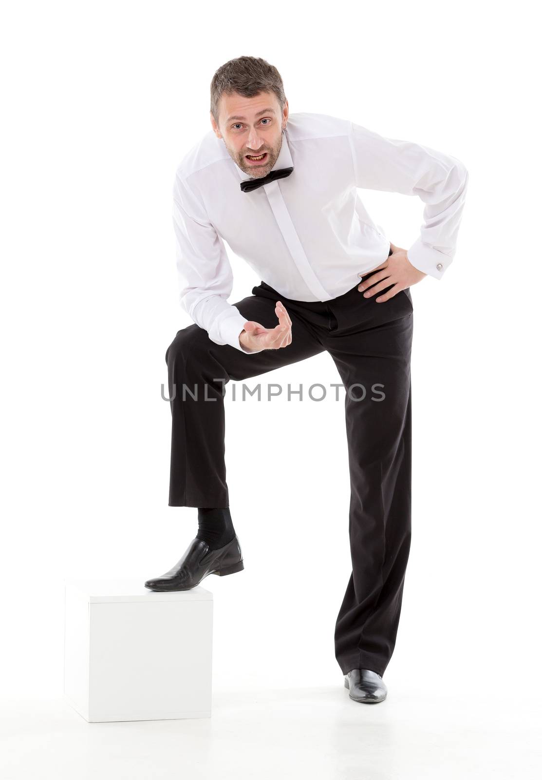 Stylish man in a bow tie leaning on a low pedestal talking to the camera while looking up and gesturing with his hand