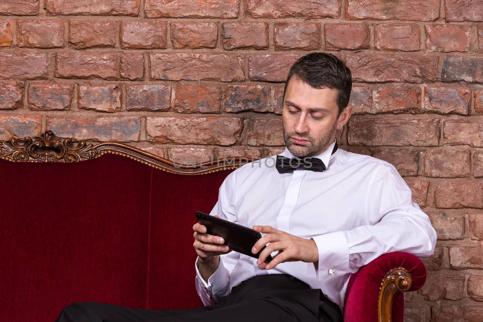 Businessman lying on a settee and reading tablet by Discovod